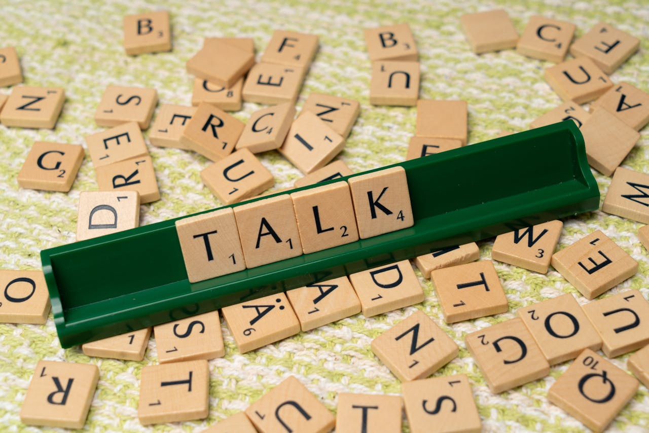 why-choose-us Scrabble tiles arranged to spell 'Talk' on a green tray, surrounded by scattered tiles on a textured surface.