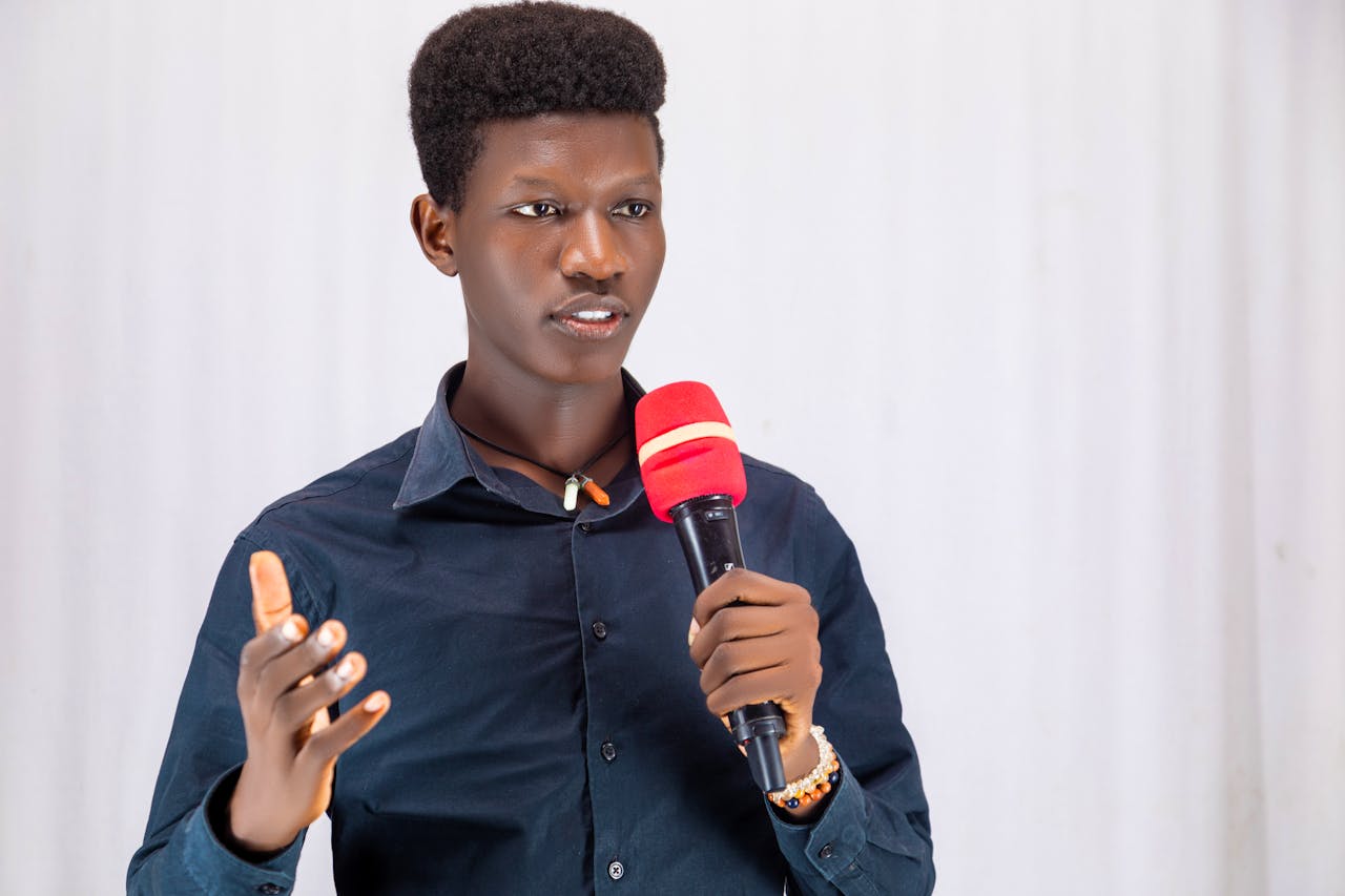 gallery-4 Confident young man presenting with a red microphone, wearing a dark shirt indoors.