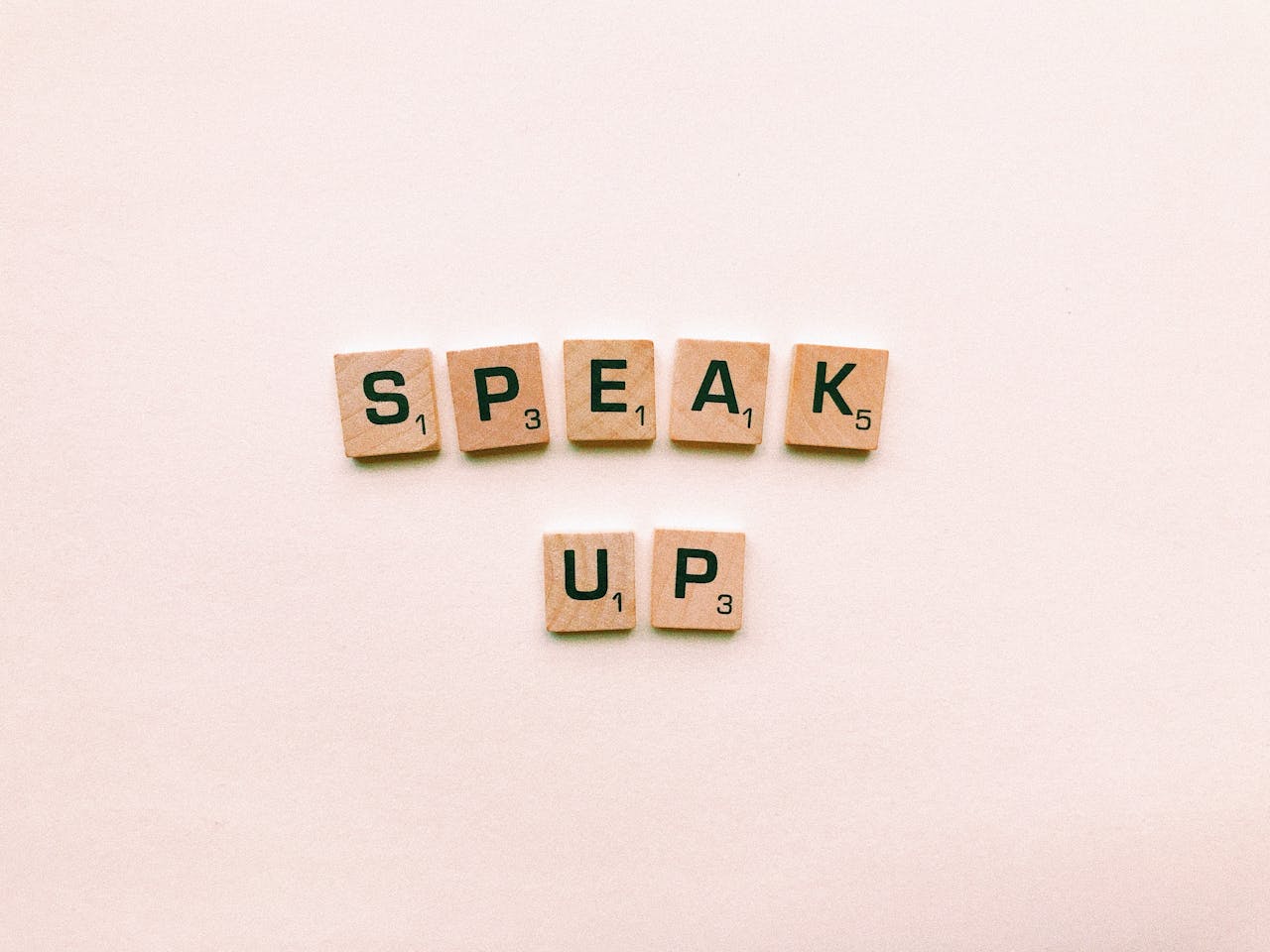 gallery-2 Wooden Scrabble tiles spelling 'Speak Up' on a pink background.