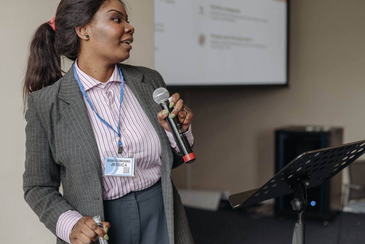 gallery-1 Woman in professional attire presenting at a business seminar with microphone.